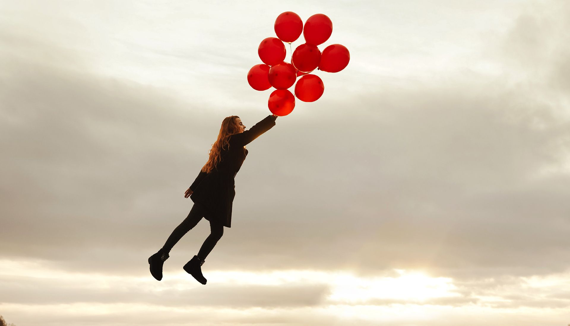 Chica volando que está sujetando un montón de globos rojos.